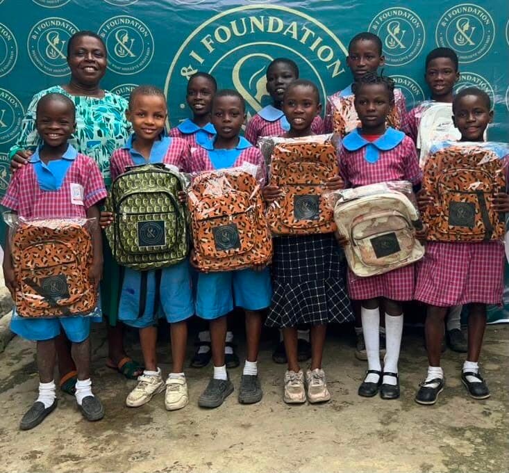 Children holding & I Foundation-branded school bags at a distribution event